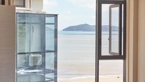 A room with a large window offering a view of a beach and distant hills.