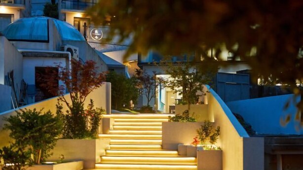 A set of outdoor stairs leading up to a building with a dome structure, surrounded by greenery and illuminated by warm lighting.