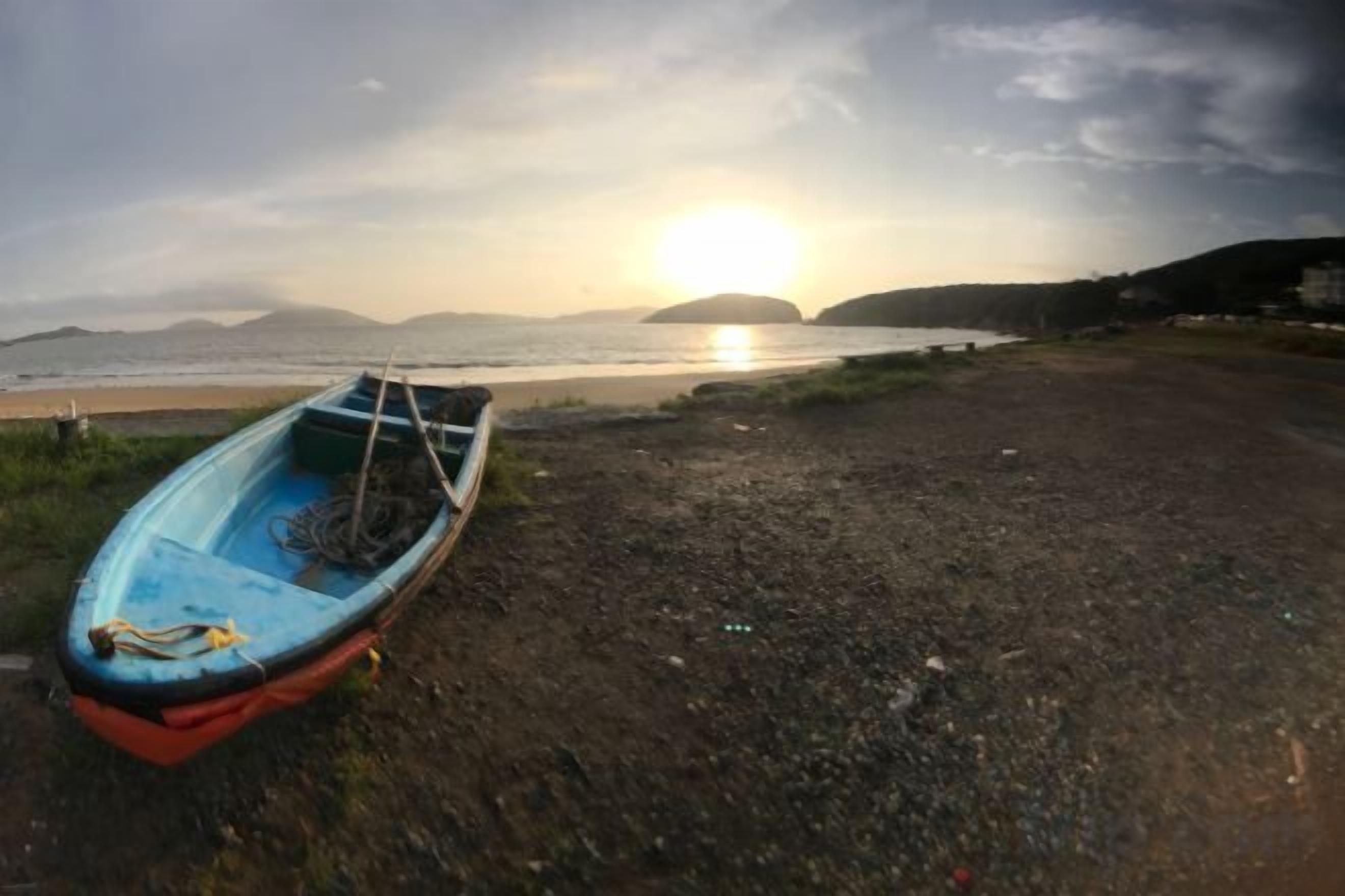 Un bote en la playa con un atardecer de fondo.