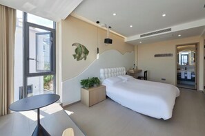 A modern hotel room with a large bed, a small bedside table with a plant, a round table, and a view through a large window. - Otter Home (Zhoushan)