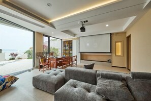 A modern living room with a large gray sectional sofa, a dining area with a wooden table and chairs, and a large flat-screen TV mounted on the wall. - Otter Home (Zhoushan)
