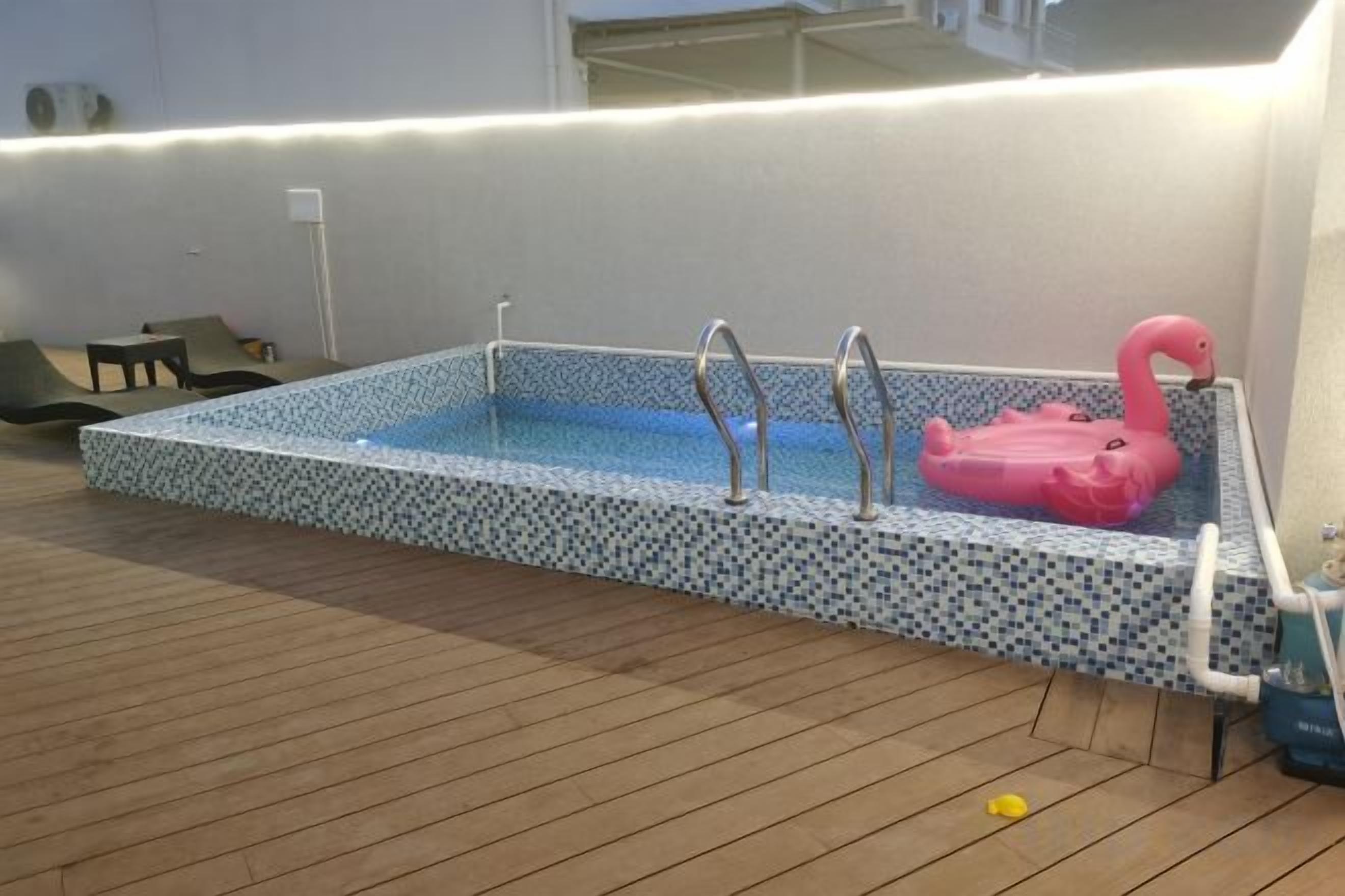 Una piscina rectangular con un flotador de flamenco rosa, escaleras metálicas y un borde con azulejos.