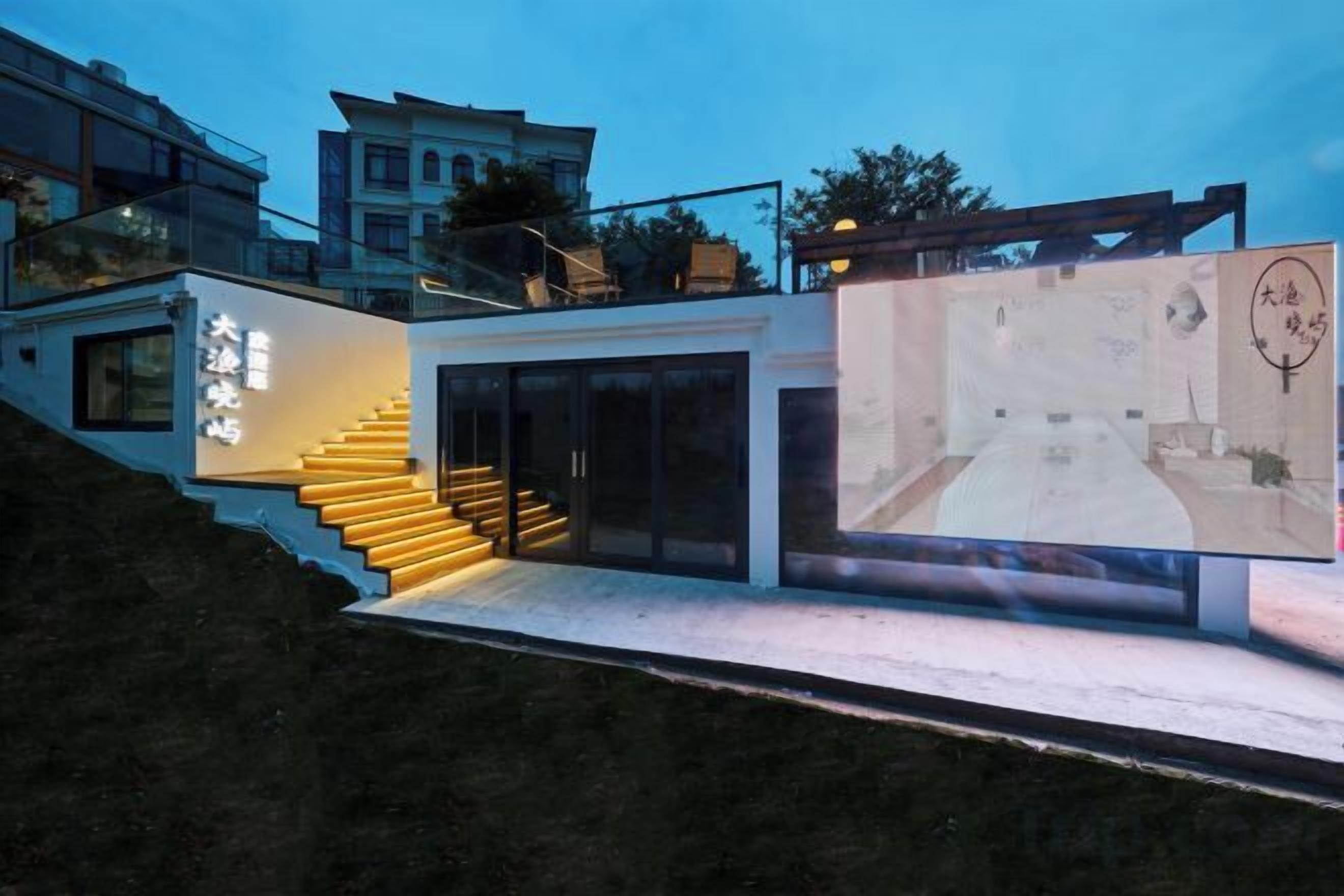 Un edificio moderno con una escalera que conduce a una puerta de cristal, un cartel grande y vistas de edificios circundantes.