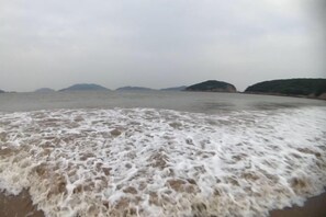 A beach with waves approaching the shore, a clear sky, and distant hills. - Otter Home (Zhoushan)