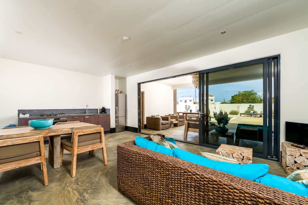 Un espace de vie moderne comprenant un coin repas, un grand canapé en osier et une porte-fenêtre coulissante donnant sur une terrasse extérieure.