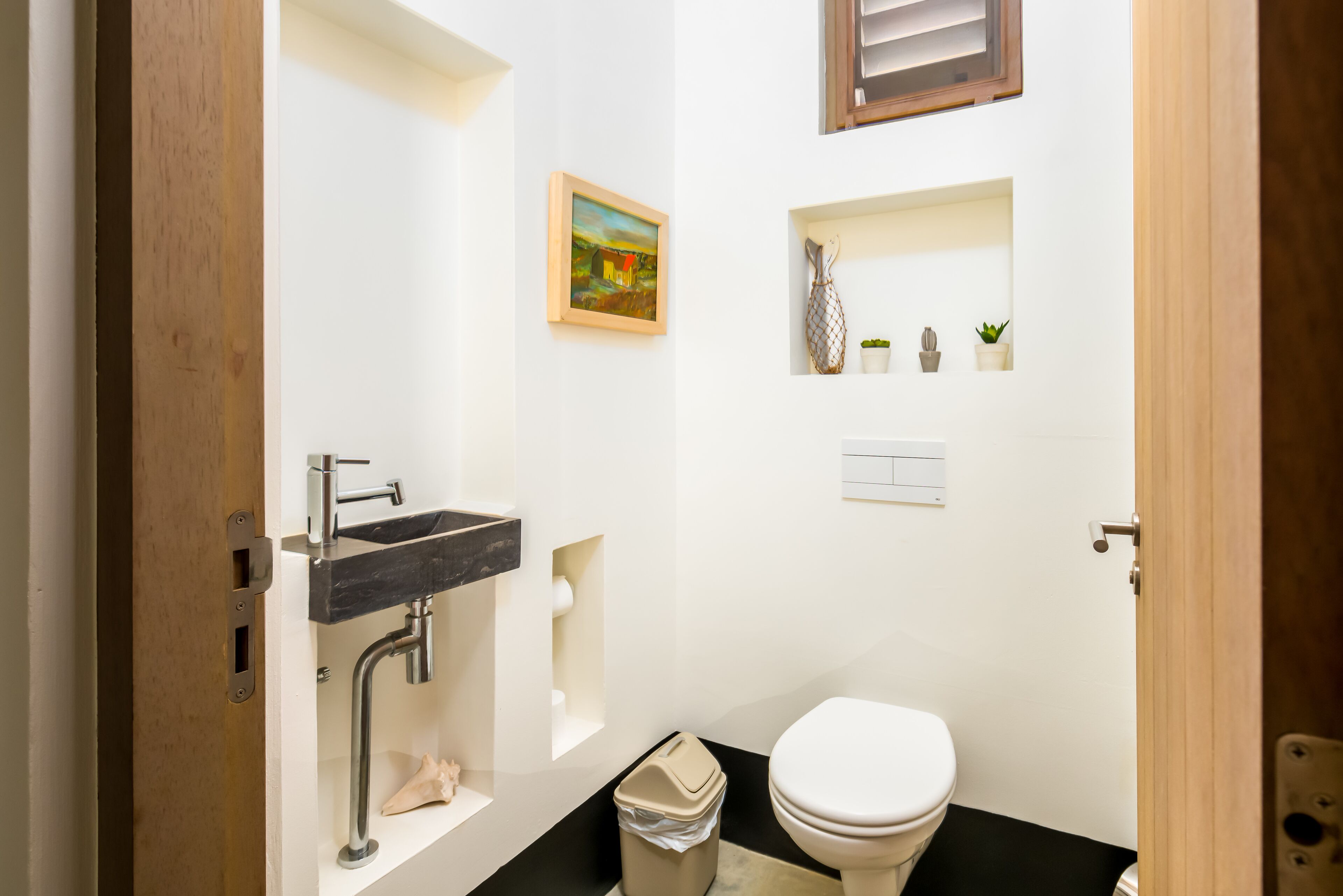 Un bagno moderno con lavandino nero, water bianco e un piccolo ripiano con oggetti decorativi.