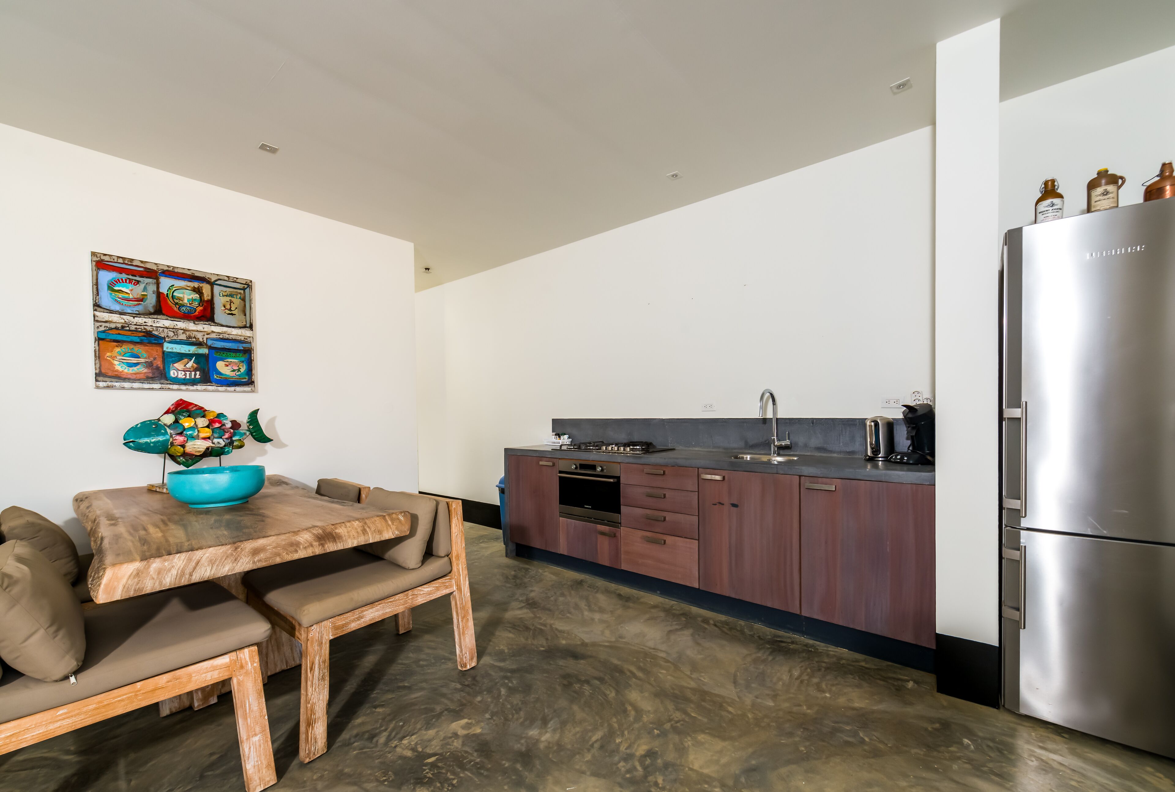 A modern kitchen with a wooden dining table, bench seating, and a stainless steel refrigerator.