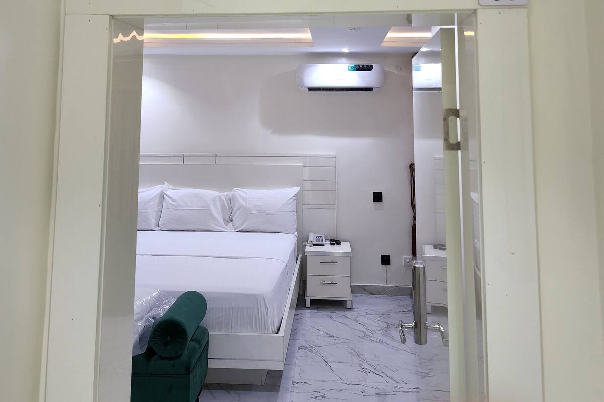 Quarto de hotel com cama, uma cadeira verde, mesa de cabeceira, banheiro e placa indicando o número do quarto 124.
