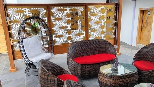 Un espace extérieur aménagé avec un toit, doté de meubles en osier et de coussins rouges, d’un paravent décoratif et d’un téléviseur fixé au mur.