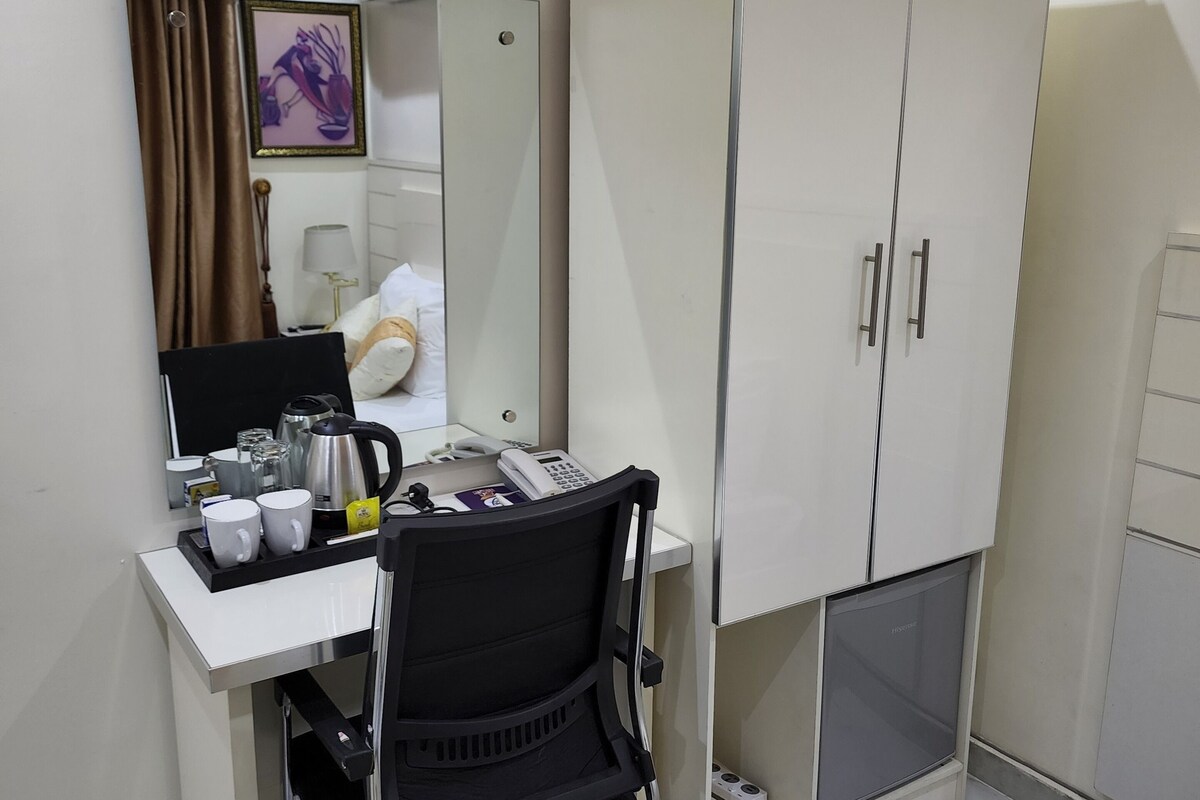A hotel room with a desk, a chair, a wardrobe, a bed, and a bathroom.