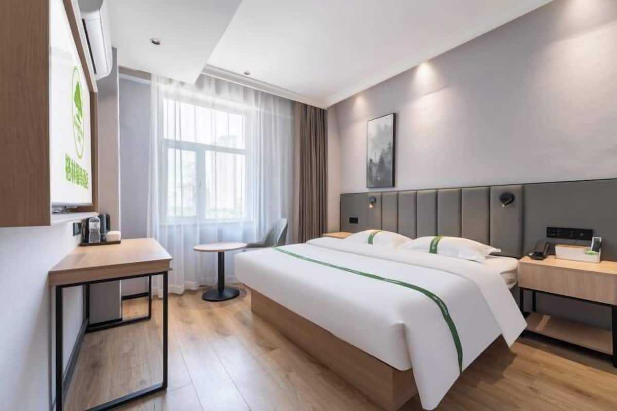 Habitació d'hotel moderna amb un llit gran, taules de nit, una taula rodona petita i una finestra amb cortines.