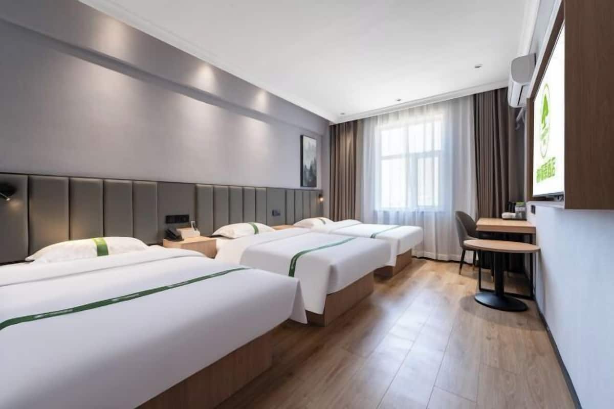 Habitació d'hotel amb tres llits, un escriptori, una cadira i una televisió.