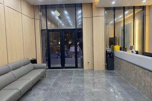 En lobby med receptionsdisk, et venteområde med sofa og en entré med glasdør.