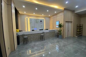 A modern reception area with a marble floor, a counter with stools, a potted plant, and a door with a sign.