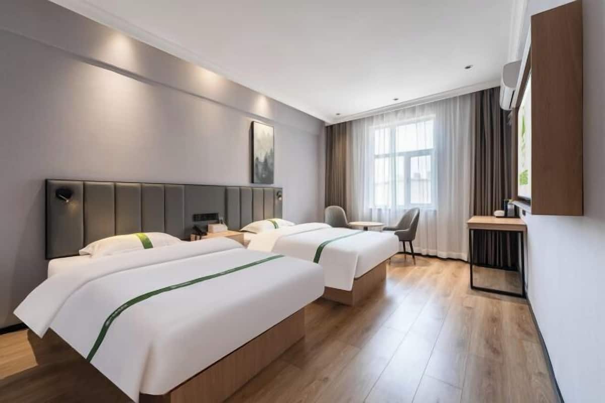Habitació d'hotel amb dos llits, un escriptori, una cadira i una finestra gran amb cortines.