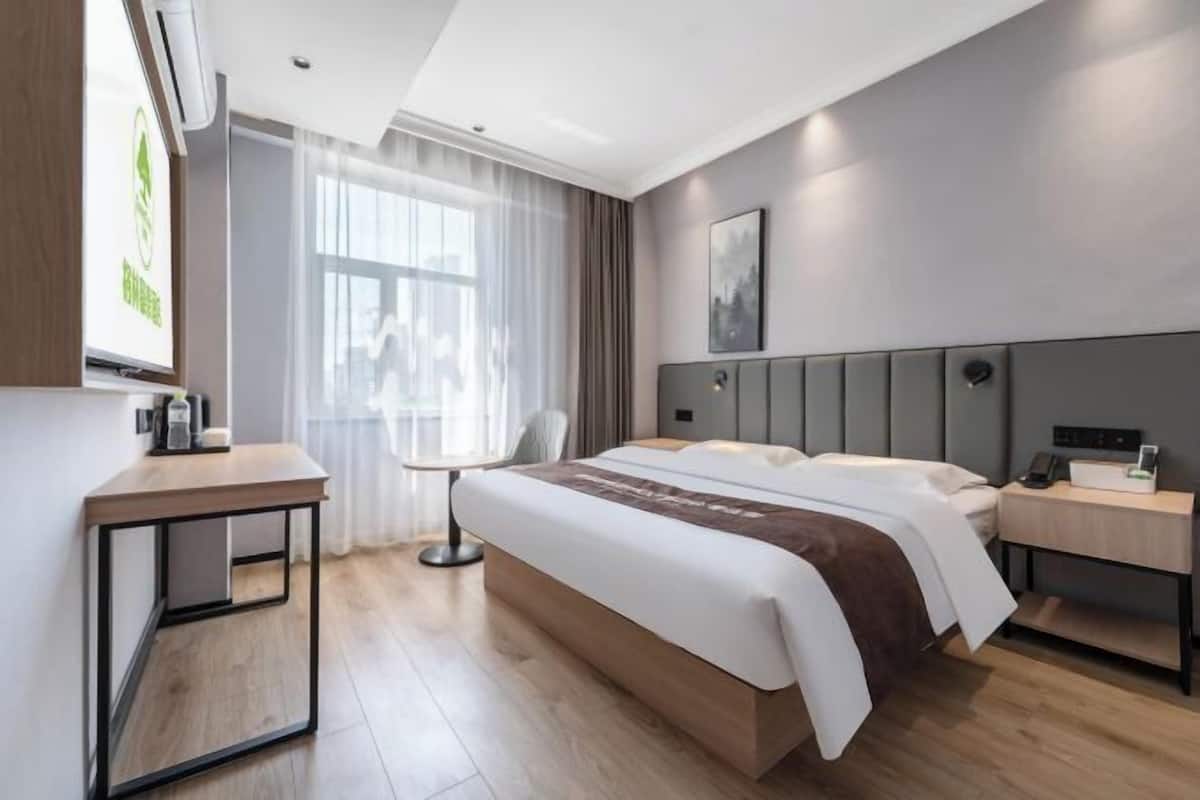 Habitació d'hotel moderna amb un llit gran, taules de nit, escriptori i finestra amb cortines.