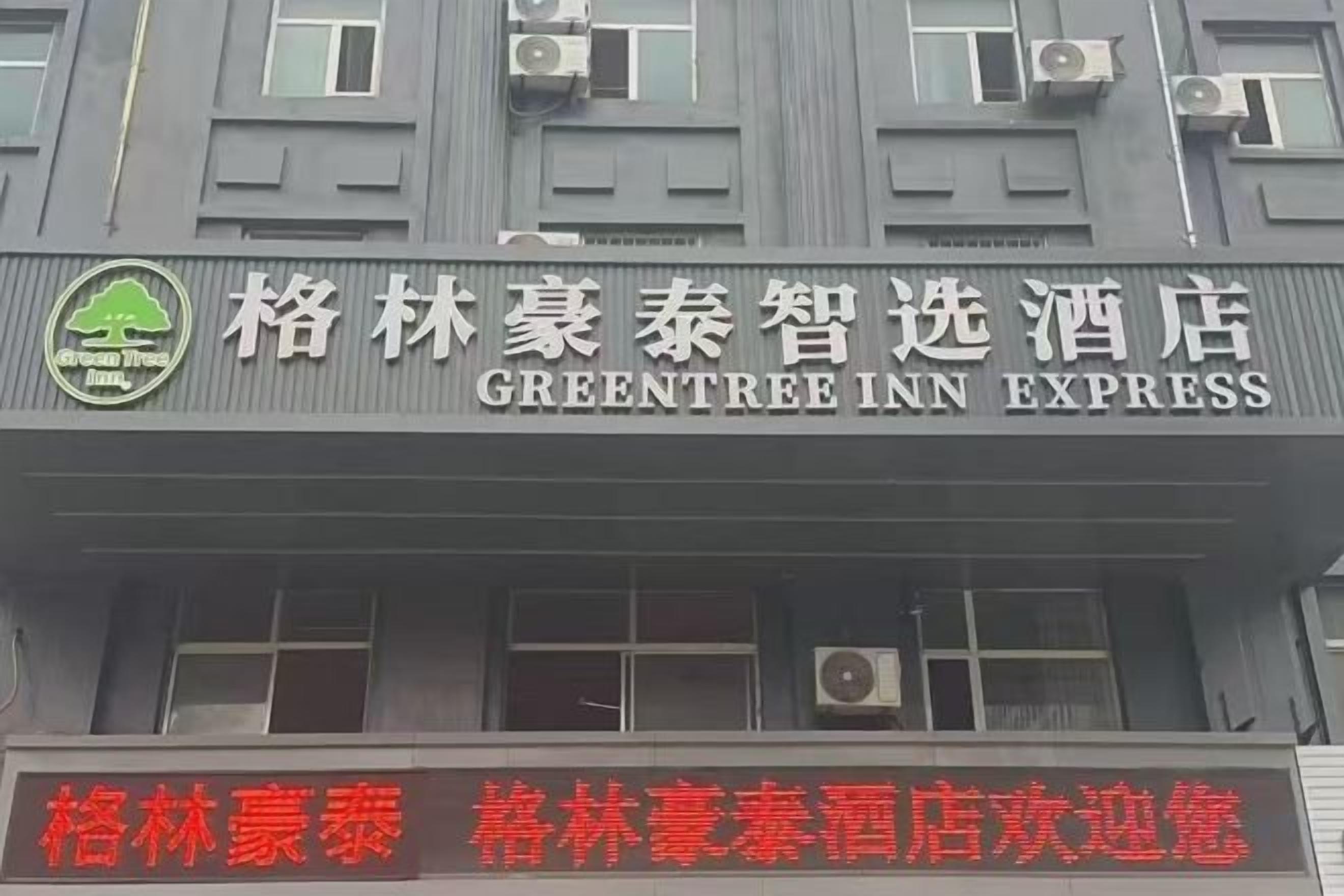 A hotel sign with the name 'GreenTree Inn Express' and a logo with a tree and a leaf.