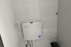 A toilet with a white tank and a blue sticker, a metal pipe, and a black trash bin. - Jinying Shanzhuang Hotel (Hengshan County)