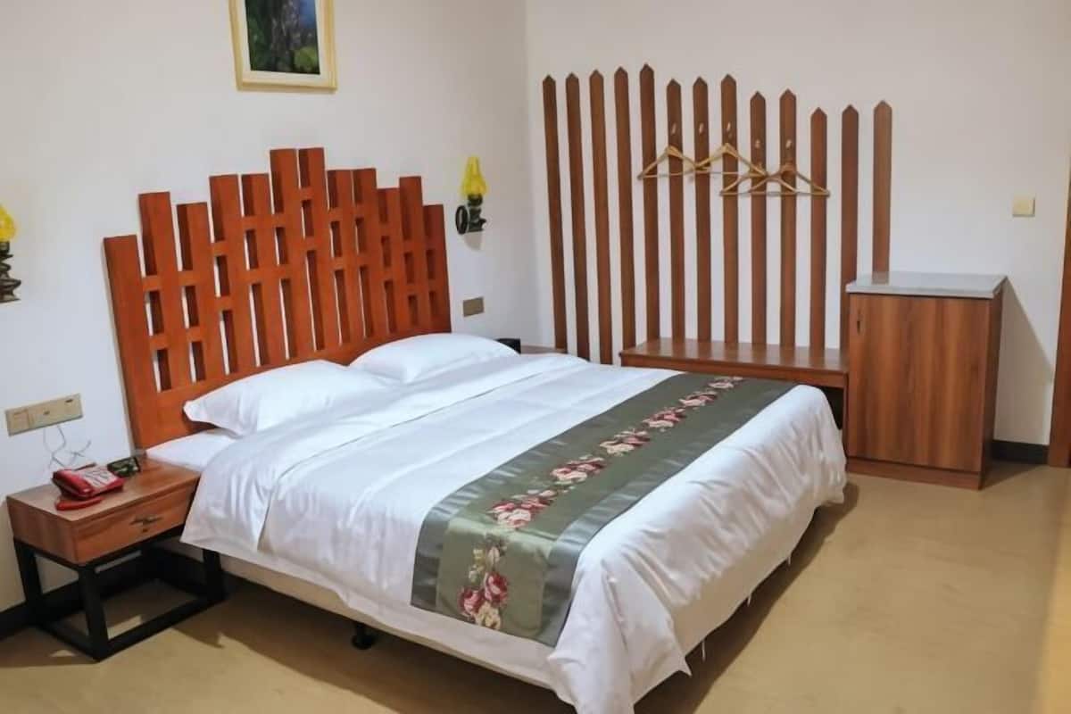 A neatly made bed with a wooden headboard, a bedside table with a lamp, and a small cabinet.