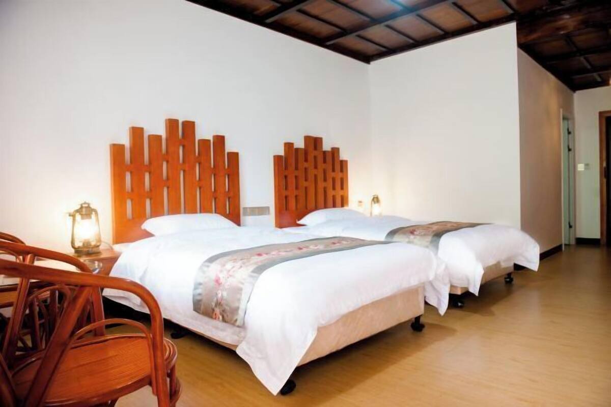 A hotel room with two beds, wooden headboards, a wooden floor, and a nightstand with a lamp.