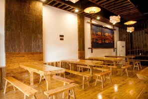 A restaurant interior with wooden tables and benches, a painting on the wall, and a wooden ceiling. - Jinying Shanzhuang Hotel (Hengshan County)