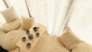 Une pièce avec une table en bois, des coussins de couleur beige et une fenêtre ornée de rideaux légers.