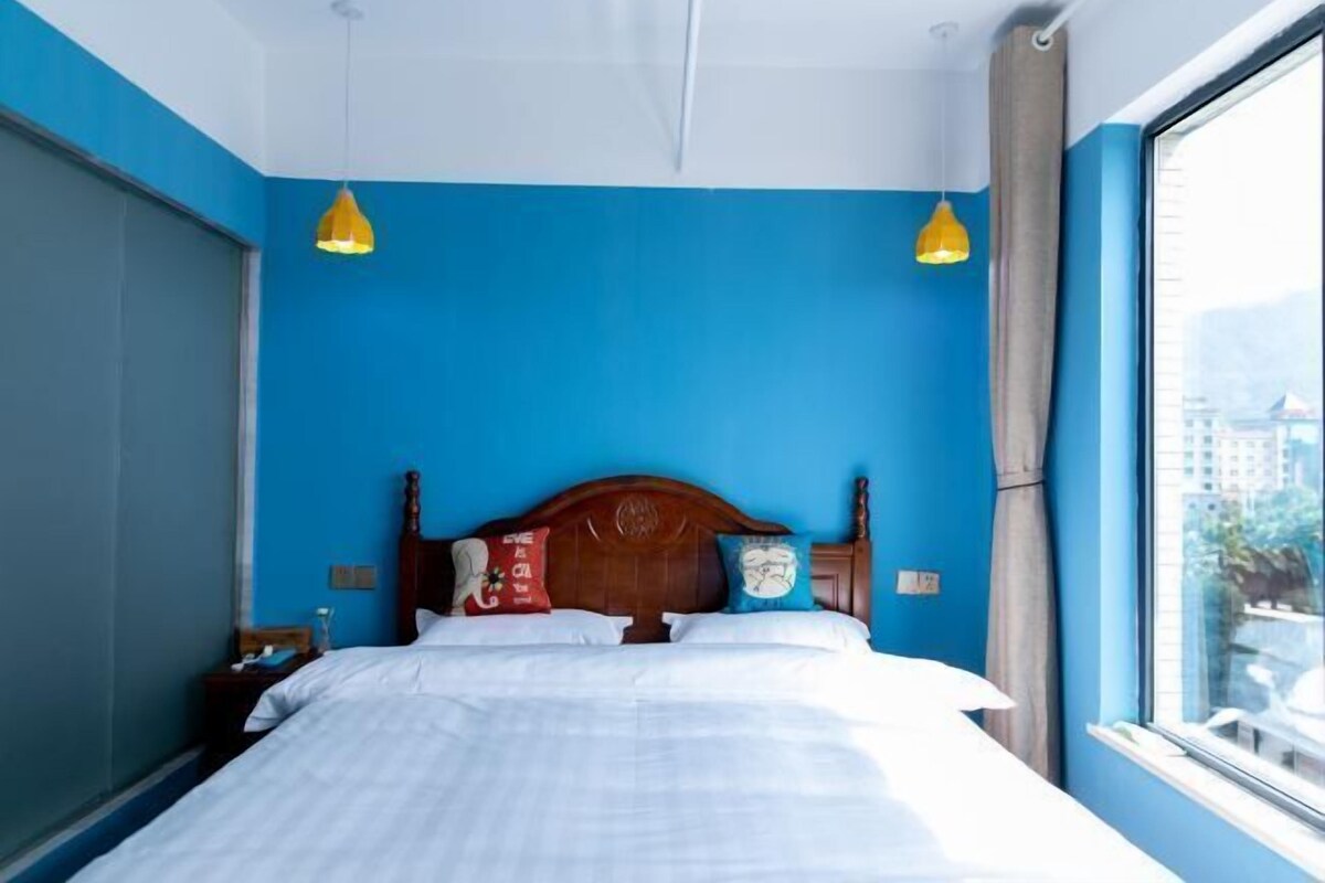 Habitación de hotel con una cama grande, dos lámparas colgantes, un cabecero de madera y una ventana con vistas.