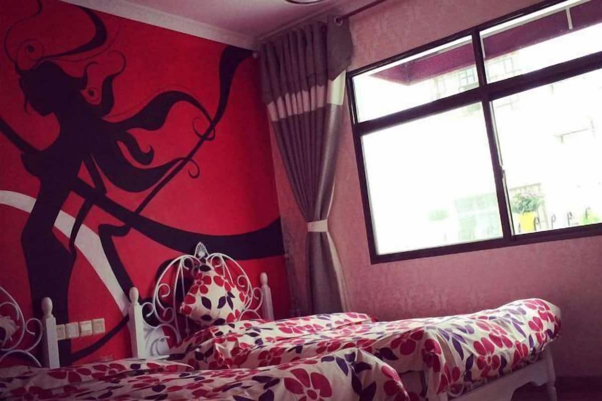 Ein Zimmer mit einem Bett, einem fensterbepflanzten Fenster und einer Wand mit einem abstrakten Rot- und Schwarzmuster.