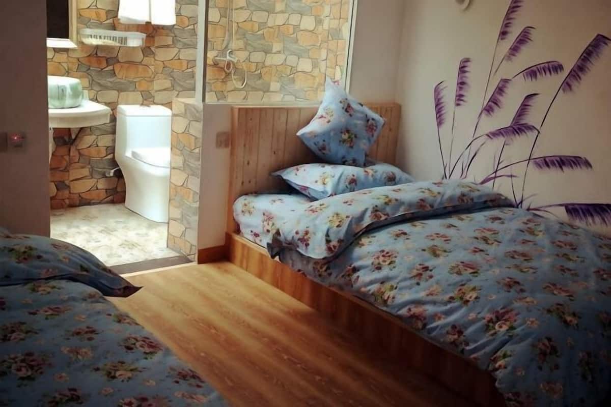 Ein Schlafzimmer mit Holzboden, einem Bett mit Blumenbettwäsche, einer Steinsturz und einem Badezimmer mit einer weißen Toilette.