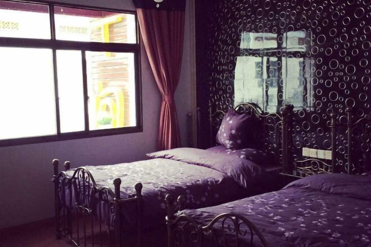 Ein Zimmer mit zwei Betten, einem Fenster mit Vorhängen und einer Wand mit Muster.