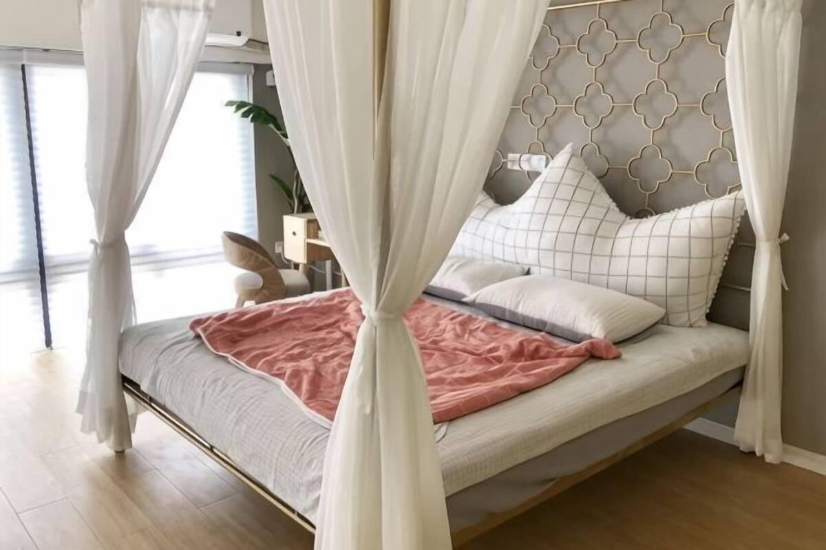 A bed with a canopy, a bedside table, and a plant.