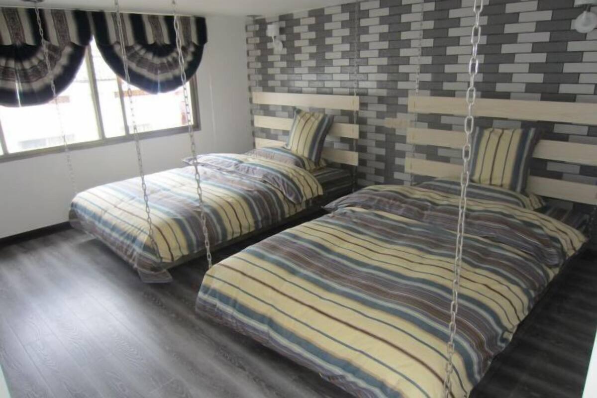 Ein Schlafzimmer mit zwei Betten, gestreifter Bettwäsche, einem Kopfende mit Ziegelmuster und einem Fenster mit Vorhängen.