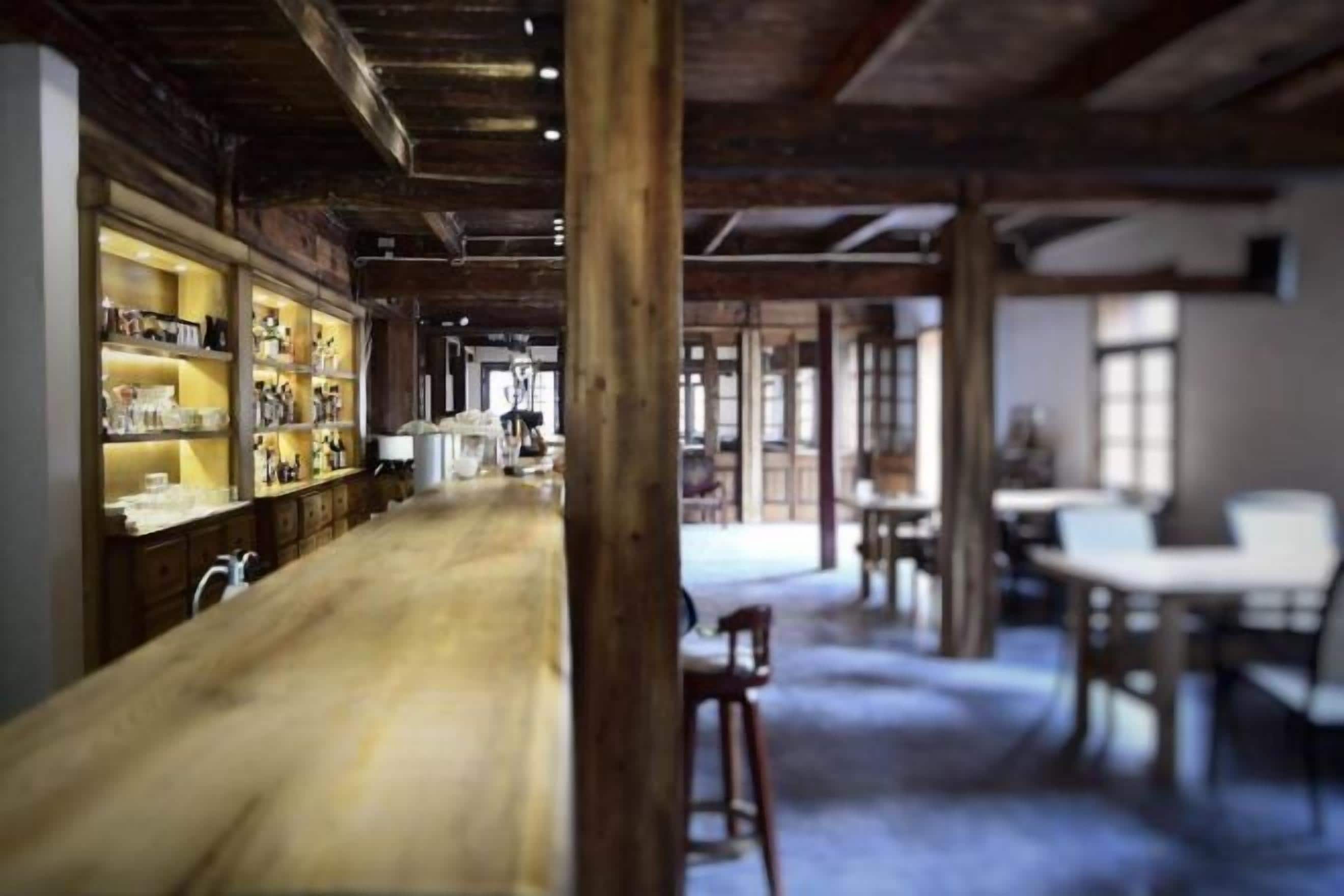 A spacious room with a long wooden table, a seating area with chairs, and a display of items on shelves.