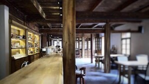 Een ruime kamer met een lange houten tafel, planken met diverse voorwerpen en een rustiek plafond.