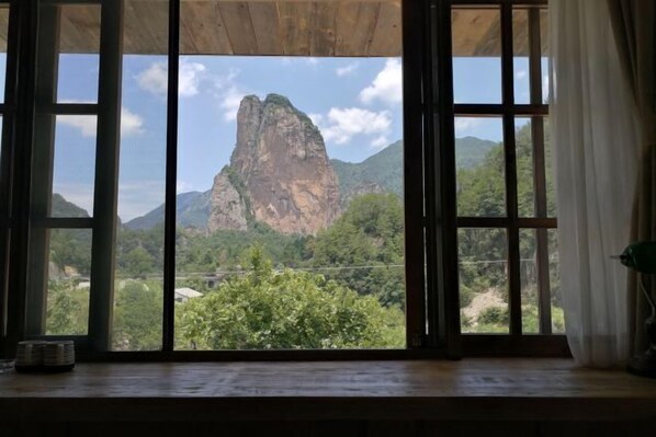 Quarto com uma janela grande que oferece vista para uma formação rochosa imponente e vegetação ao redor.