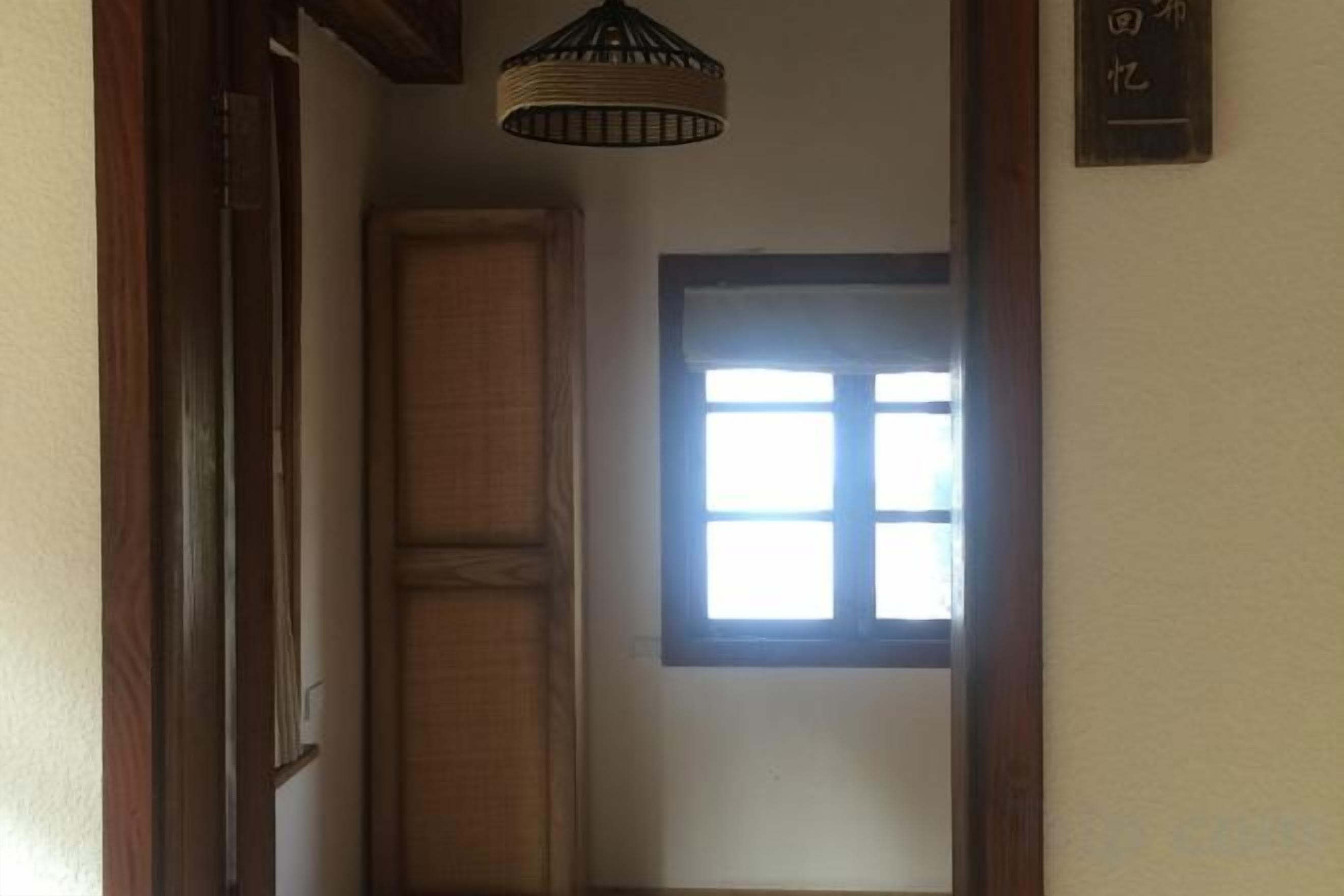 Ein schmaler Flur mit einer Holztür und einem Fenster mit Gittermuster.