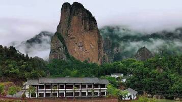 A building with a traditional architectural style, surrounded by lush greenery and a prominent rock formation in the background.