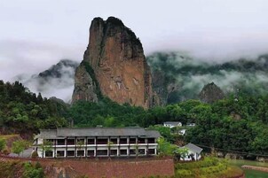 Un edificio de estilo arquitectónico tradicional, rodeado de exuberante vegetación y una imponente formación rocosa al fondo.