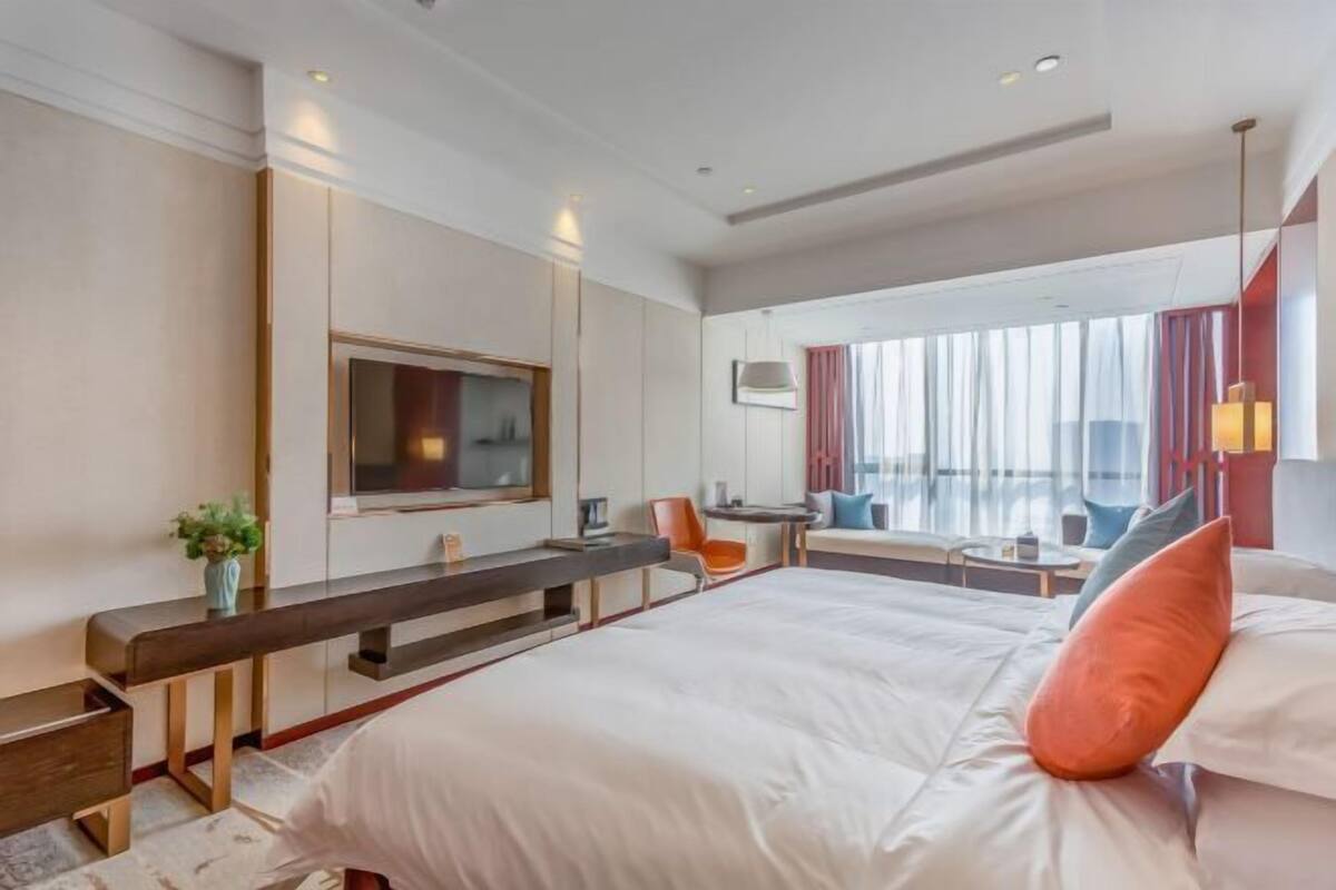 Habitación de hotel moderna con una cama grande, un escritorio, un televisor y una zona de estar con vistas a la ciudad.