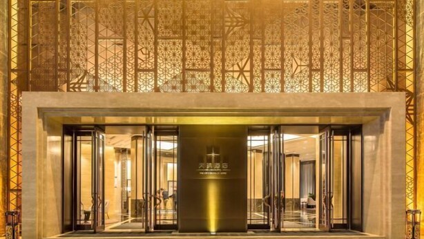 L’entrée d’un hôtel au design moderne, avec un pilier central orné de texte, des portes en verre et un plafond à motifs.