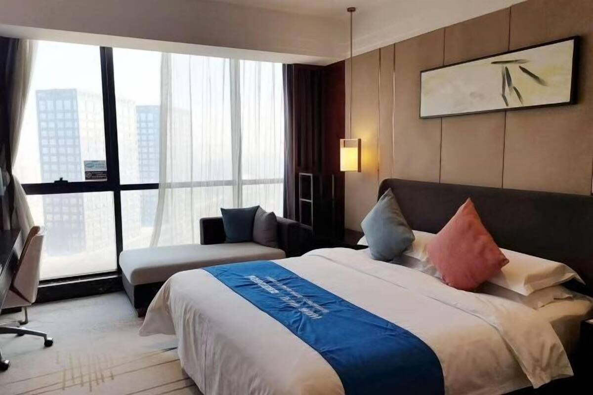 Habitación de hotel con una cama grande, un escritorio, una silla, un sofá, una ventana con vistas a la ciudad y una obra de arte colgada en la pared.
