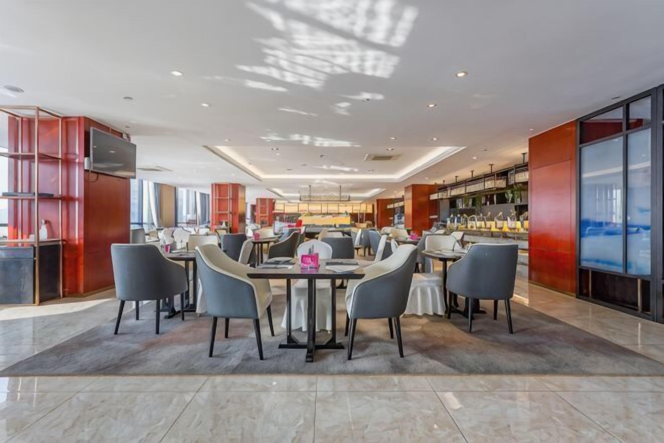 Eine großzügige Hotelhalle mit einem zentralen Essbereich, einer Bar und einem großen Fernsehbildschirm.