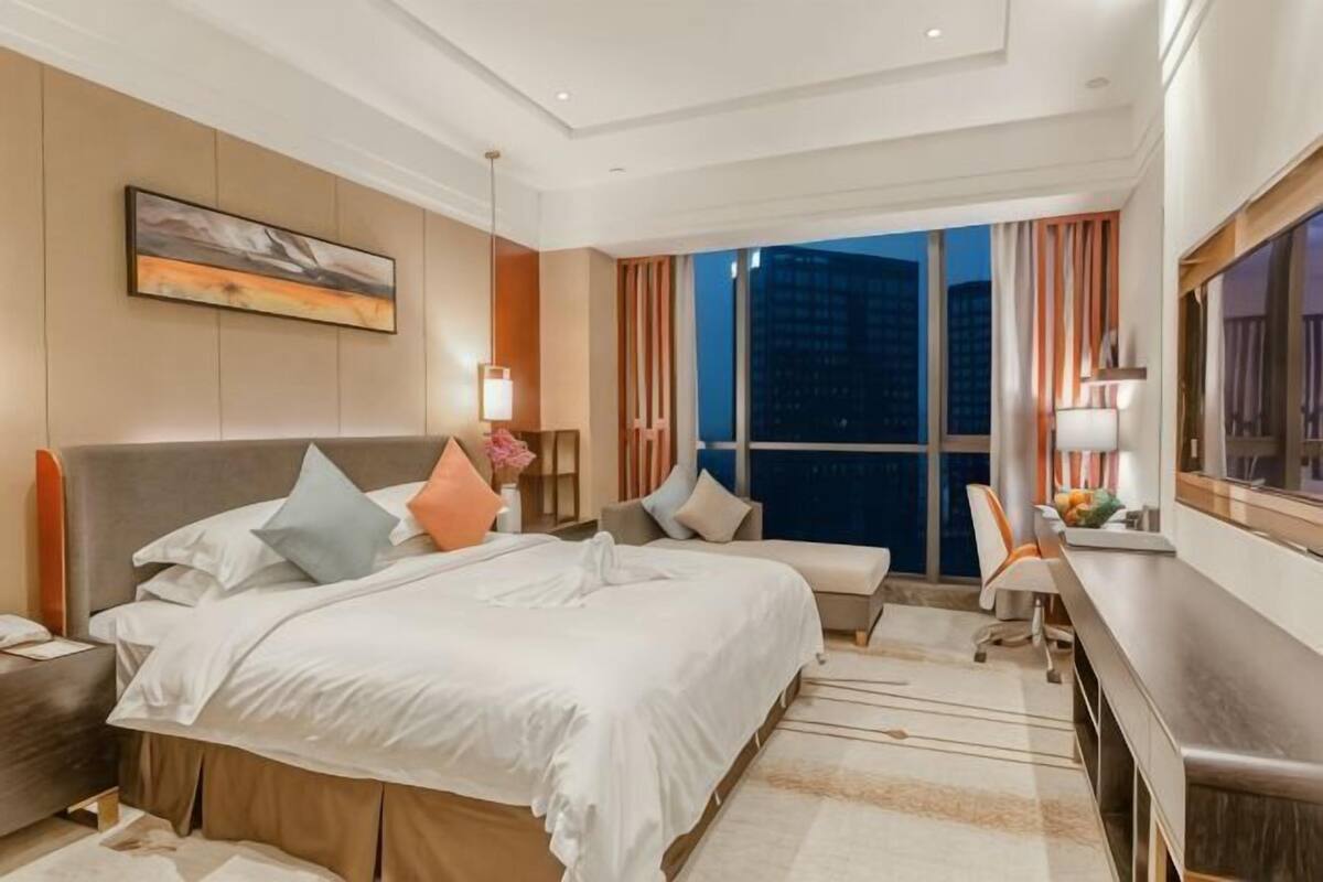 Una habitación de hotel con una cama grande, un escritorio, una silla, una mesita de noche y un ventanal con vistas a la ciudad.