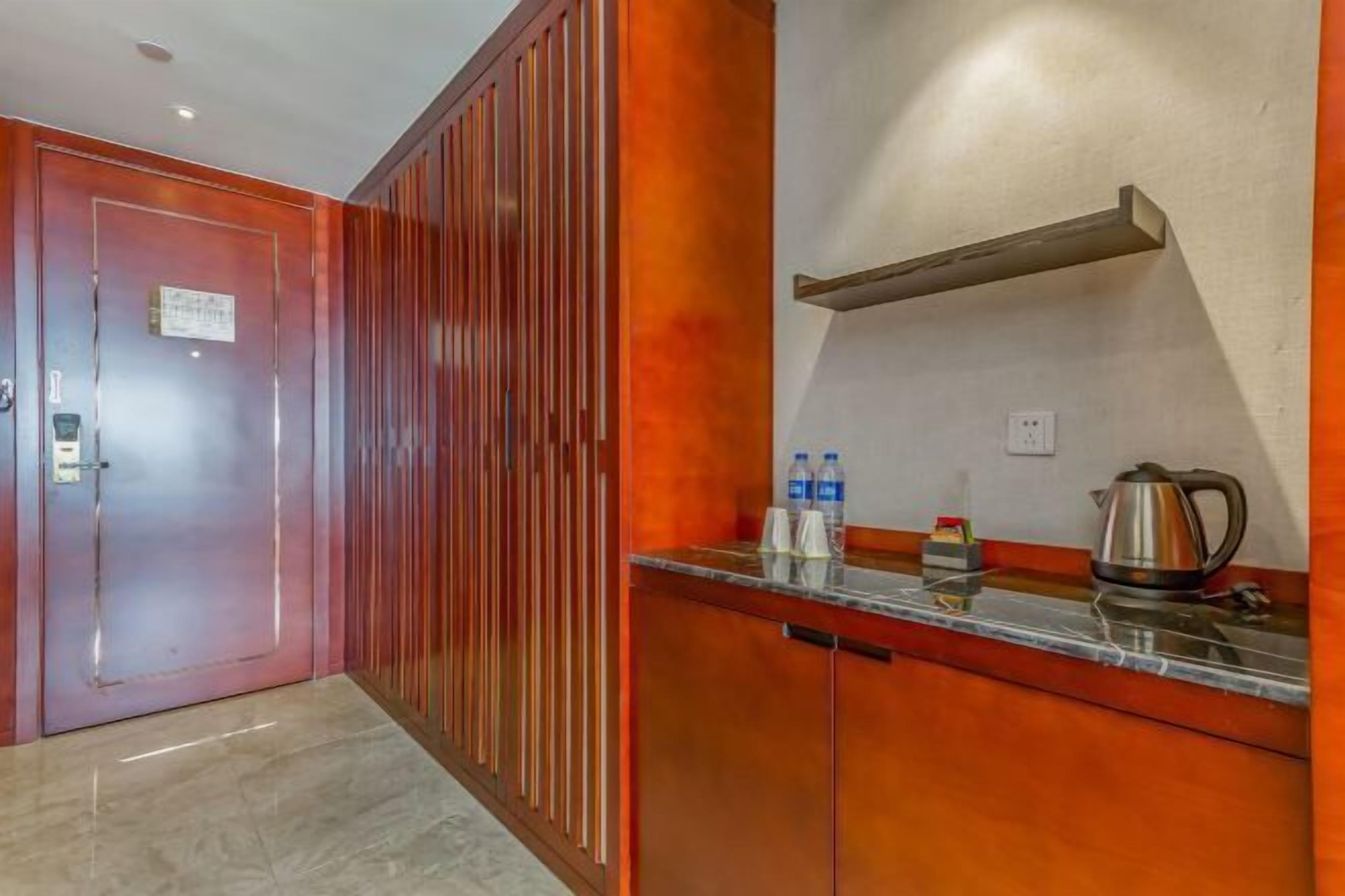A hotel corridor with a wooden door, a metal radiator, and a countertop with a kettle and bottles.