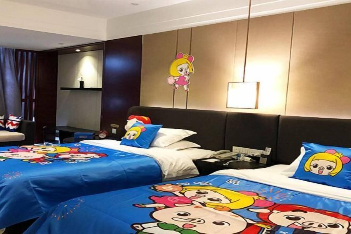 Una habitación de hotel con dos camas, cada una con ropa de cama de temática de dibujos animados. Hay un estante montado en la pared con una lámpara, un espejo grande y un adorno mural.