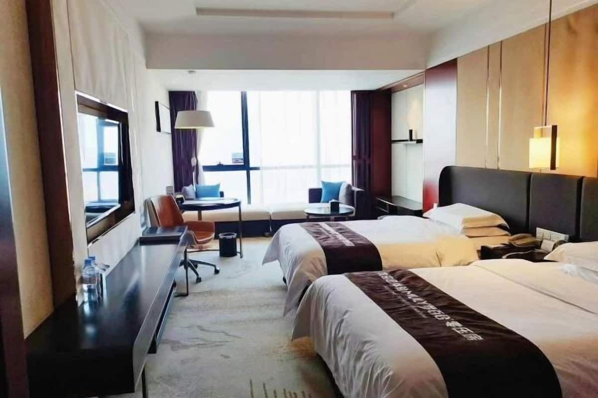 Habitación de hotel con dos camas, un escritorio, una silla, una mesita, una lámpara y una ventana.