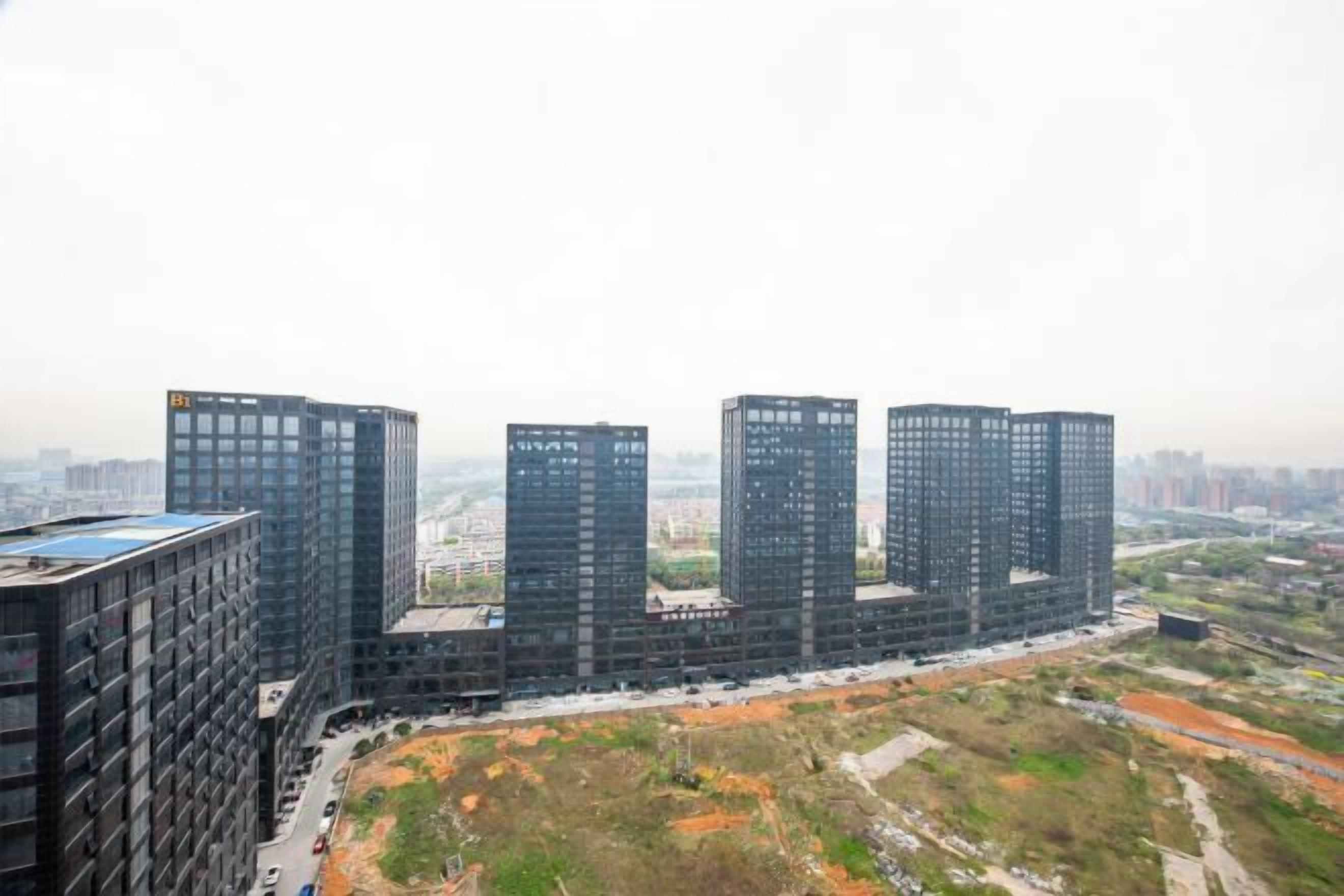 A high-rise building complex with multiple skyscrapers, surrounded by construction sites and open land.