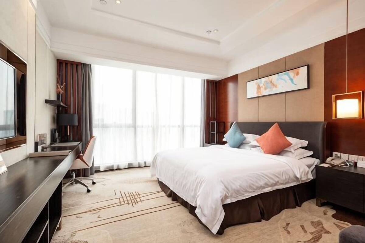Habitación de hotel con una cama grande, un escritorio, una silla, un televisor y una ventana con cortinas.