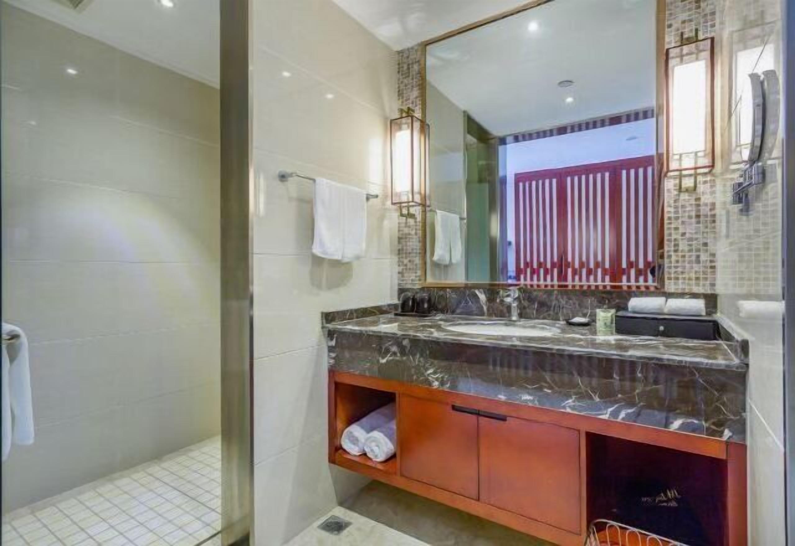Un baño moderno con cabina de ducha de vidrio, tocador de mármol con lavabo y un espejo grande.