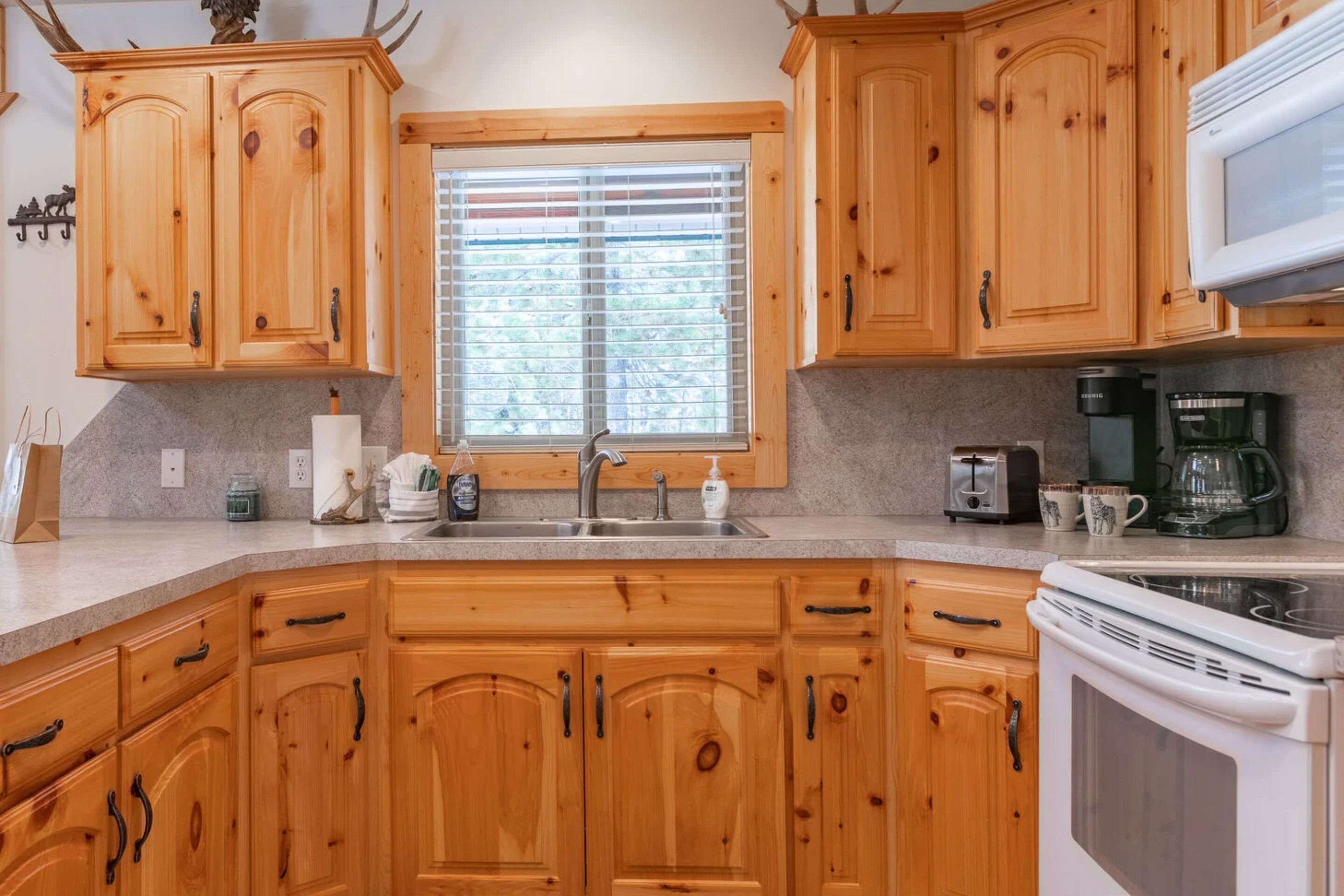 A kitchen with wooden cabinets, a sink, a stove, and a window with blinds.